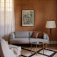 Black-framed Corporis in Bloom artwork displayed above a gray sofa on a wood-paneled living room wall.
