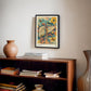 Black-framed Hepar in Bloom artwork displayed above a wooden bookcase with books and a ceramic vase.