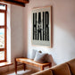 Oak-framed HAIR artwork with silver scissors hanging above a wooden bench in a sunlit room.