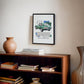 Black-framed 1961 Jaguar E-Type art print hanging above a wooden bookcase.
