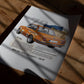 Unframed orange BMW 2002 art print lying on a wooden surface in patterned sunlight.