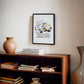 Black-framed 1985 Lamborghini Countach artwork hanging above a wooden bookcase.