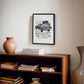 Black-framed 1969 Chevrolet Camaro collage artwork displayed above a wooden bookcase with books and a ceramic vase.