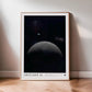 Light wood-framed Artemis II art print showing a crescent Earth above the lunar horizon, leaning against a wall on a wooden floor.