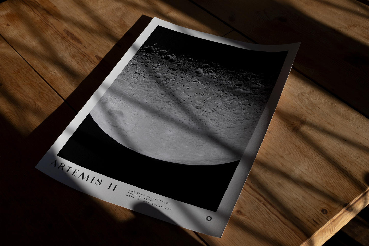 Unframed Artemis II lunar surface art print lying on a wooden table in patterned sunlight.