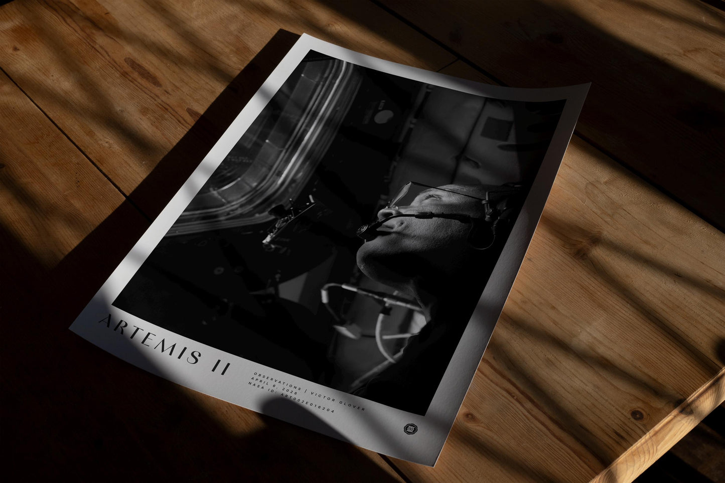 Unframed Artemis II astronaut art print lying on a wooden table in dramatic sunlight and shadow.