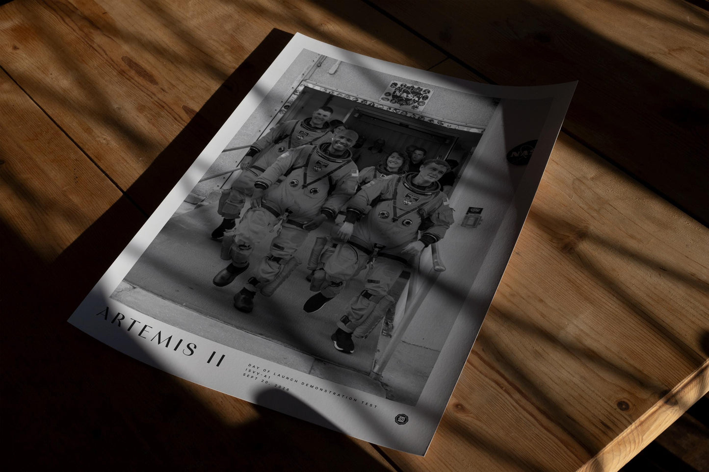 Unframed Artemis II crew art print lying on a wooden table in dappled sunlight.
