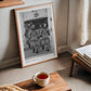 Oak-framed Artemis II crew art print leaning beside a window in a living room with a cup of tea in the foreground.