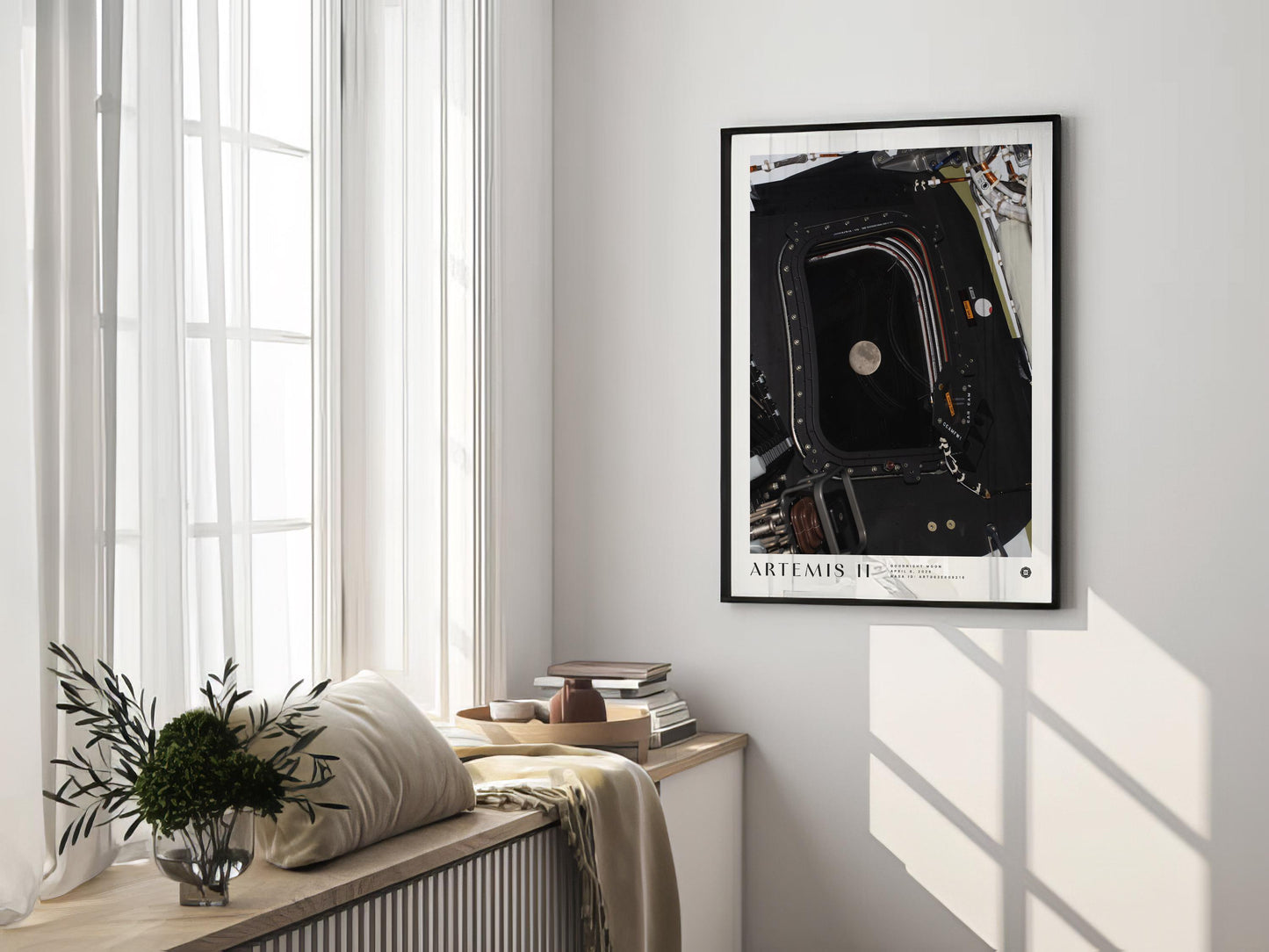 Black-framed Artemis II Goodnight Moon art print hanging in a sunlit room above a window bench with cushions, books, and flowers.
