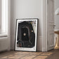 Black-framed Artemis II Goodnight Moon art print leaning against a wall in a bright room beside a window and open doorway.