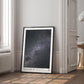 Black-framed Artemis II Starstruck art print leaning against the wall in a bright room beside a window and open doorway.