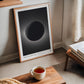 Oak-framed Artemis II eclipse artwork leaning beside a window, books, and a cup of tea.
