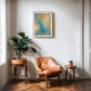 Oak-framed teal and yellow abstract “Get back to center” art print above a tan leather chair and plants.