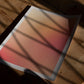 Unframed Good energy only gradient art print lying on a wooden floor beneath leafy shadows