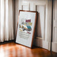 Dark wood-framed 1965 Porsche 911 collage artwork leaning against a paneled wall beside a curtained window.