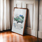 Dark wood-framed 1961 Jaguar E-Type art print leaning beside a curtained window.