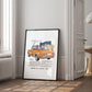 Black-framed orange BMW 2002 artwork leaning against a paneled wall beside a window and open doorway.