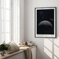 Black-framed Artemis II lunar horizon art print displayed on the wall of a sunlit room beside tall windows and a cushioned bench.