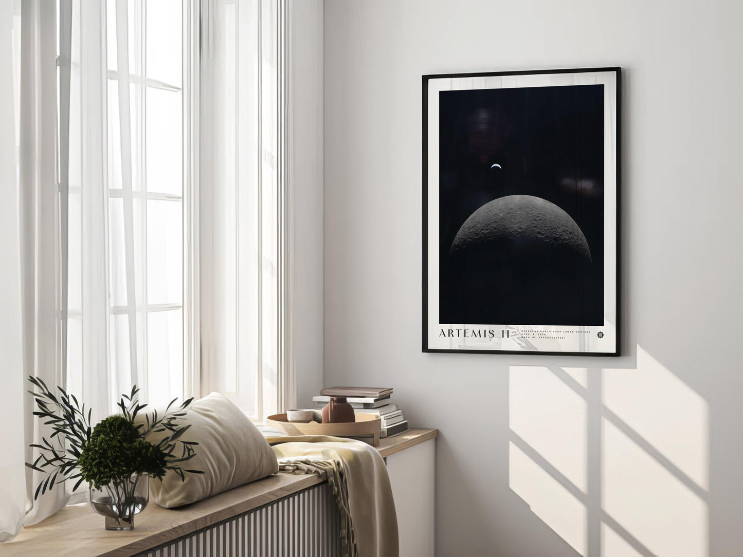 Black-framed Artemis II lunar horizon art print displayed on the wall of a sunlit room beside tall windows and a cushioned bench.