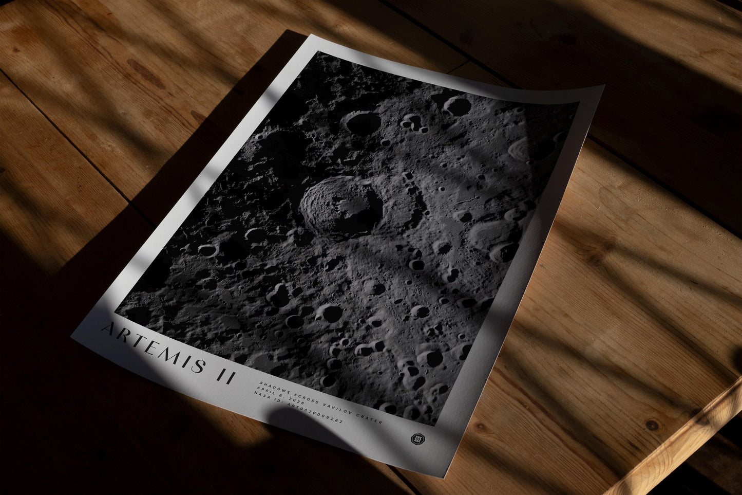 Unframed Artemis II Shadows Across Vavilov Crater art print lying on a wooden floor in dramatic window shadows.