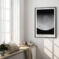 Black-framed Artemis II lunar surface art print displayed on a sunlit wall above a cushioned window seat.