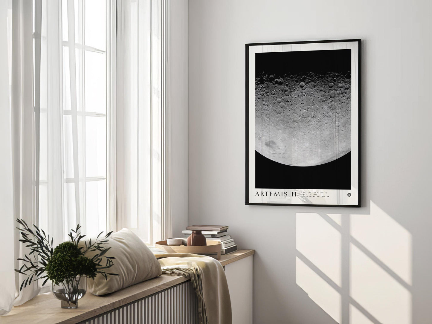 Black-framed Artemis II lunar surface art print displayed on a sunlit wall above a cushioned window seat.