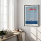 Black-framed Artemis II Orion capsule recovery art print displayed on a sunlit wall above a window seat.