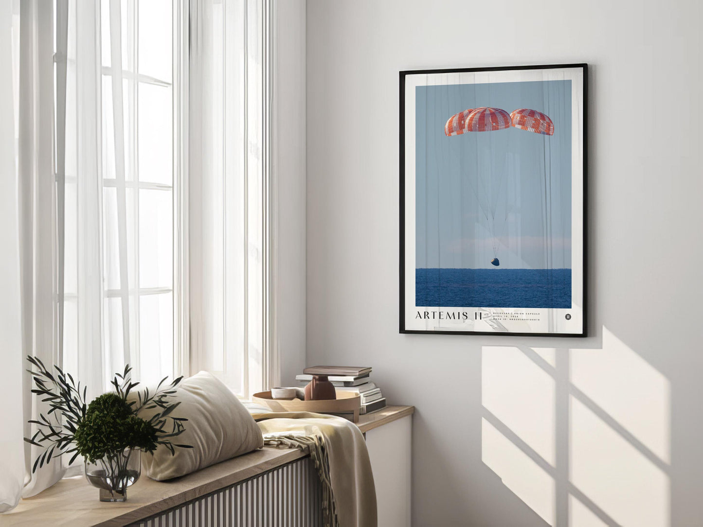 Black-framed Artemis II Orion capsule recovery art print displayed on a sunlit wall above a window seat.