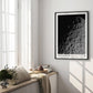 Black-framed Artemis II lunar surface art print hanging in a sunlit room above a window bench with cushions, books, and flowers.