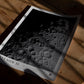 Unframed Artemis II lunar surface art print lying on a wooden table in dramatic sunlight and shadow.