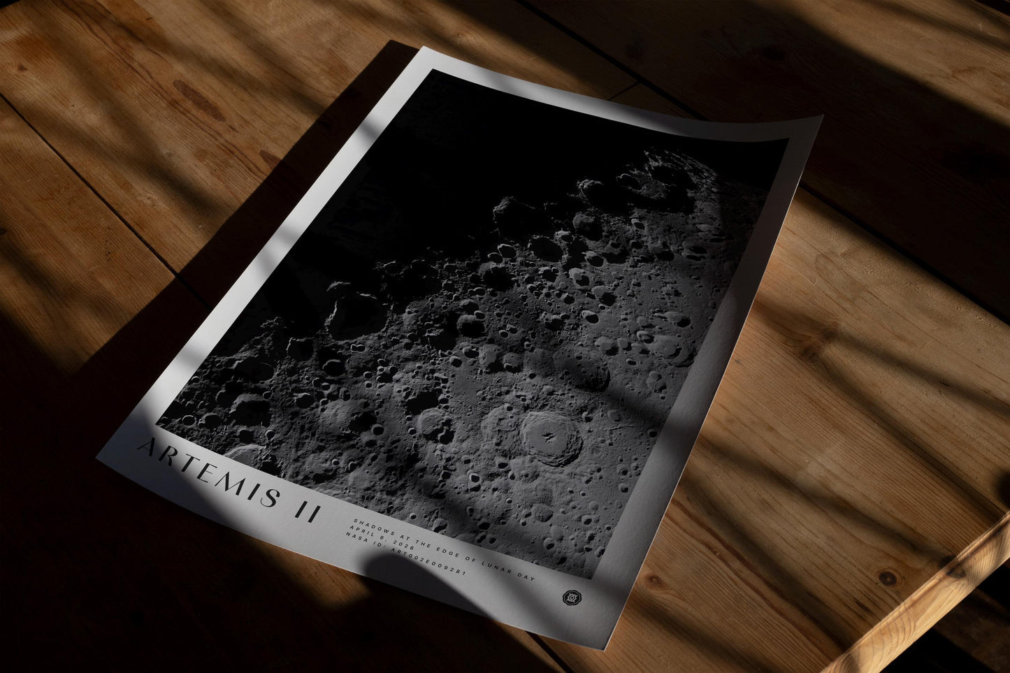 Unframed Artemis II lunar surface art print lying on a wooden table in dramatic sunlight and shadow.