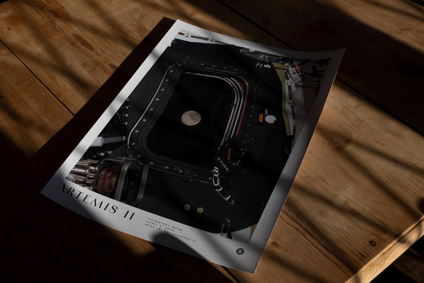 Unframed Artemis II Goodnight Moon art print lying on a wooden floor in dramatic window shadows.