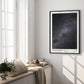 Black-framed Artemis II Starstruck art print displayed on the wall of a sunlit room beside tall windows and a cushioned bench.