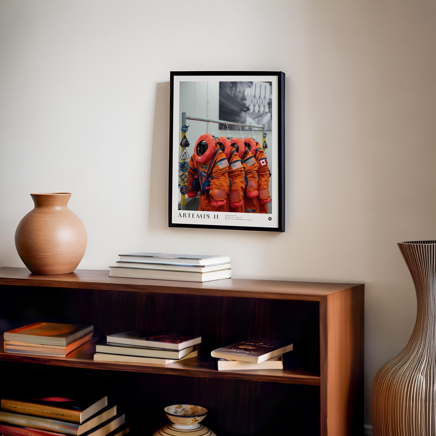 Black-framed Artemis II crew-suit art print displayed above a wooden bookcase with books and pottery.