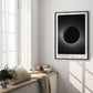 Black-framed Artemis II eclipse artwork displayed in a bright room above a cushioned window bench.