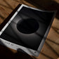 Unframed Artemis II eclipse art print lying in patterned sunlight on a wooden floor.