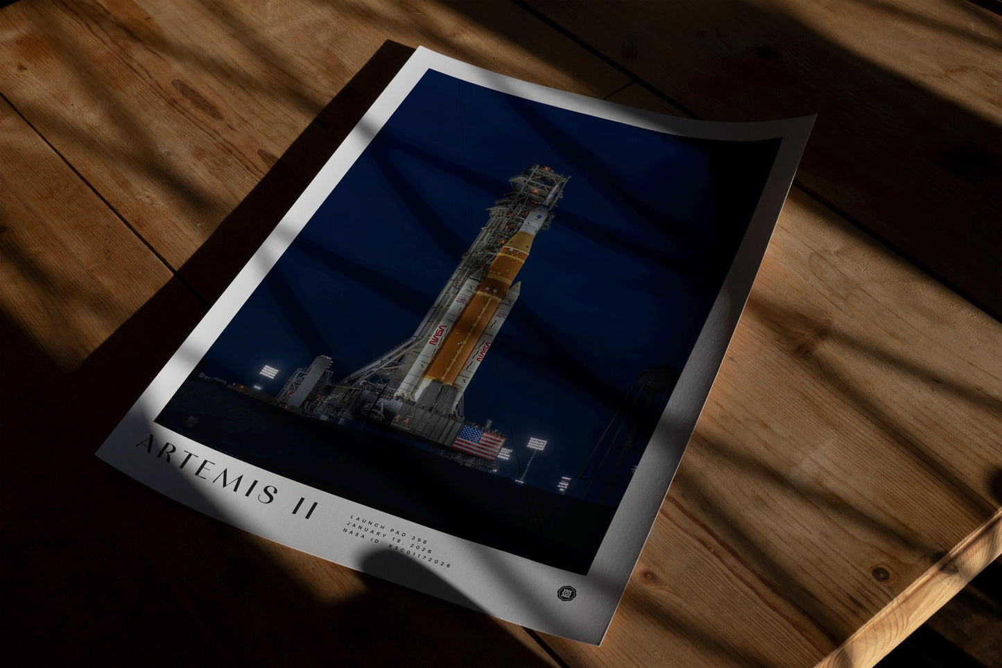 Unframed Artemis II rocket art print lying on a wooden table in patterned sunlight.