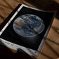 Unframed Artemis II Earth art print lying on a wooden floor in dramatic window shadows.