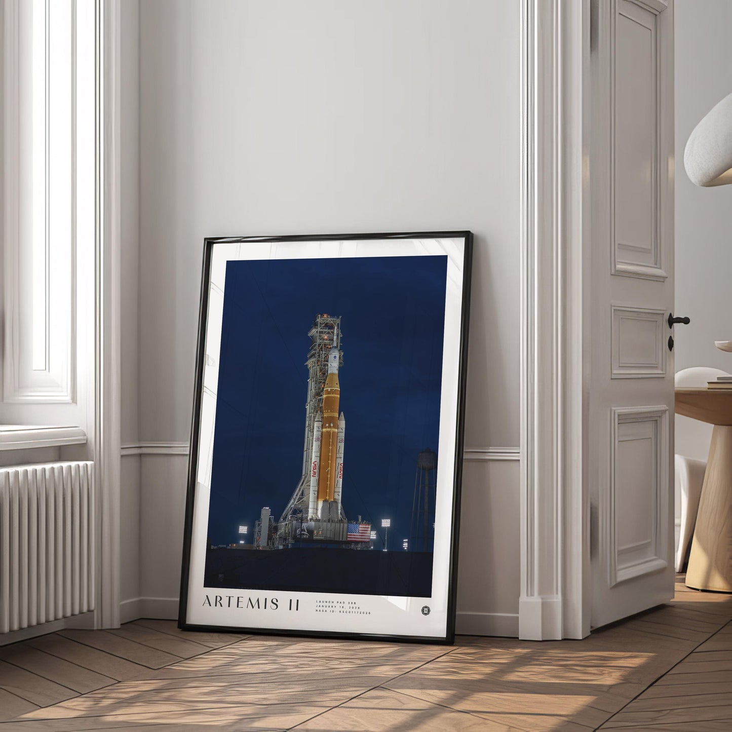 Black-framed Artemis II rocket art print leaning beside a window in a bright interior.