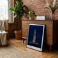 Black-framed Artemis II rocket art print leaning against a wood cabinet in a brick-walled living room.