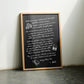 Oak-framed black dining-themed artwork leaning between leather chairs.