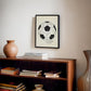 Black-framed 1930 World Cup opening match diagram artwork displayed above a wooden bookcase with books and a ceramic vase.