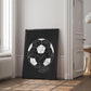 Black-framed soccer diagram artwork leaning against a paneled wall beside a window and open doorway.