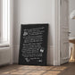Black-framed black dining-themed artwork leaning beside a doorway in a sunlit room.