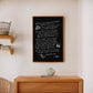 Oak-framed black dining-themed artwork hanging above a wooden console and ceramic vase.