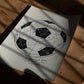 Unframed black-and-white soccer ball diagram art print resting on a sunlit wooden table.
