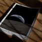 Unframed Artemis II Earthset art print lying on a wooden floor in dappled sunlight.