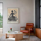 Framed Lady Justice artwork displayed in a living room above a round coffee table beside a rust-colored armchair.